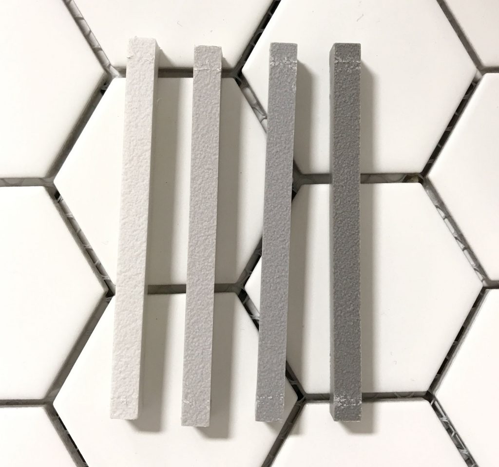 four mapei grout sample sticks atop white hex tile going from light to dark