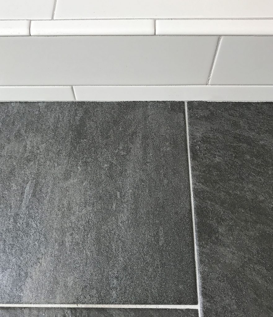 white subway tile shower next to dark slate floor with same gray grout