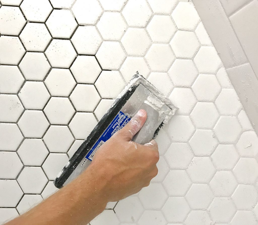 Spreading grout into white hex tile with grout float