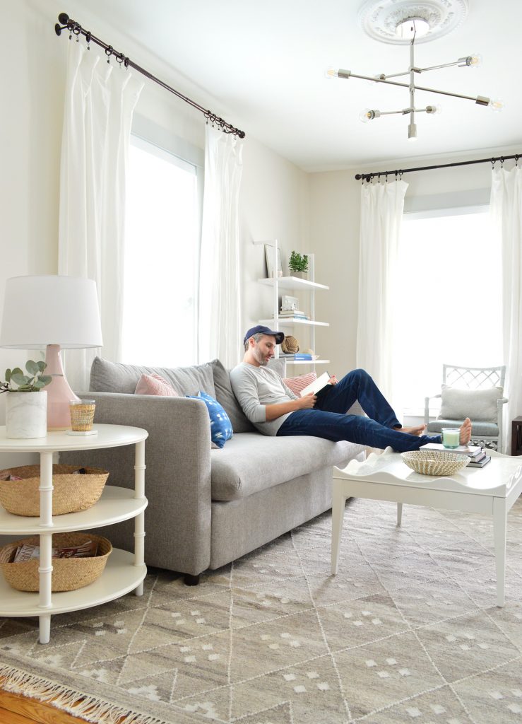 John reading on gray sofa with feet on scalloped white coffee table