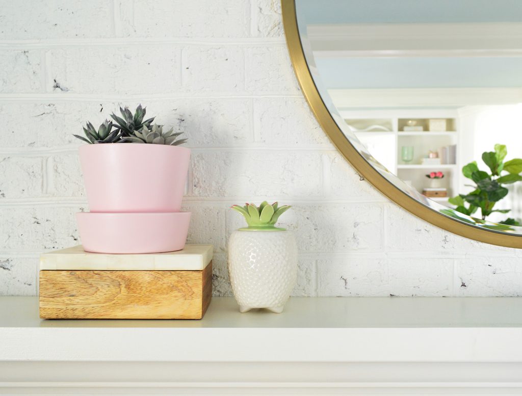 Faux succulents on living room fireplace mantle next to round gold mirror