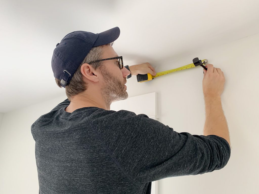 John measuring wall above window while holding curtain rod hook