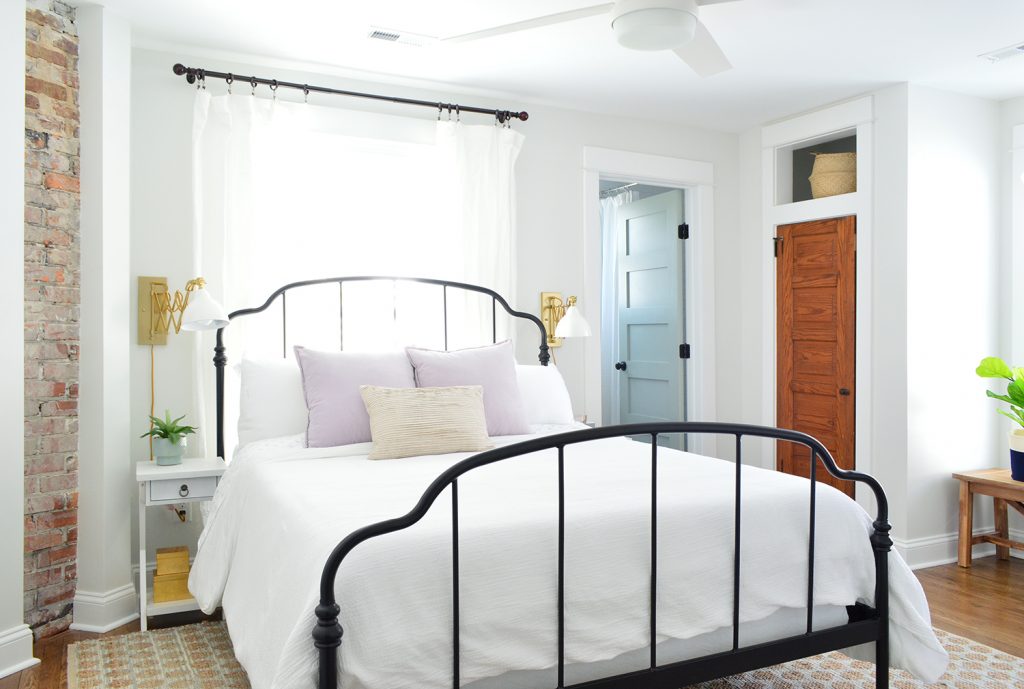 Exposed Brick Fireplace In Duplex Main Bedroom With Iron Bedframe And White Bedding