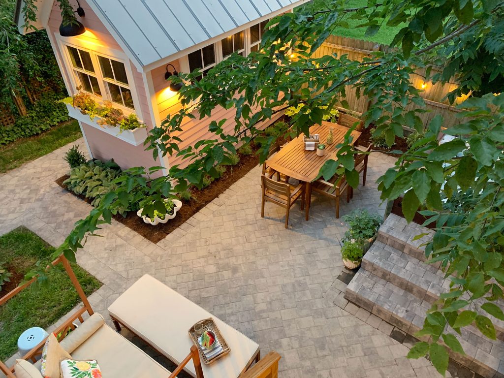 Overhead View Of Beach House Backyard At Dusk With String Lights And Outdoor Table And Lounge Furniture