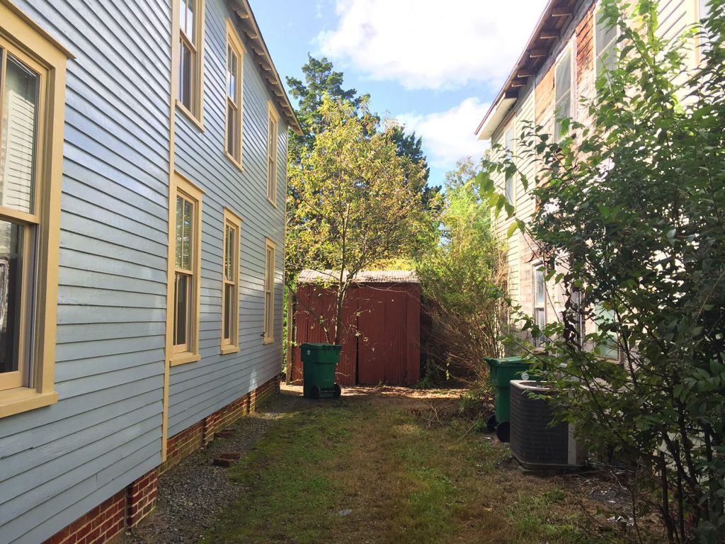 Before View Down Side Yard Of Beach House With Rusted Shed And Trees