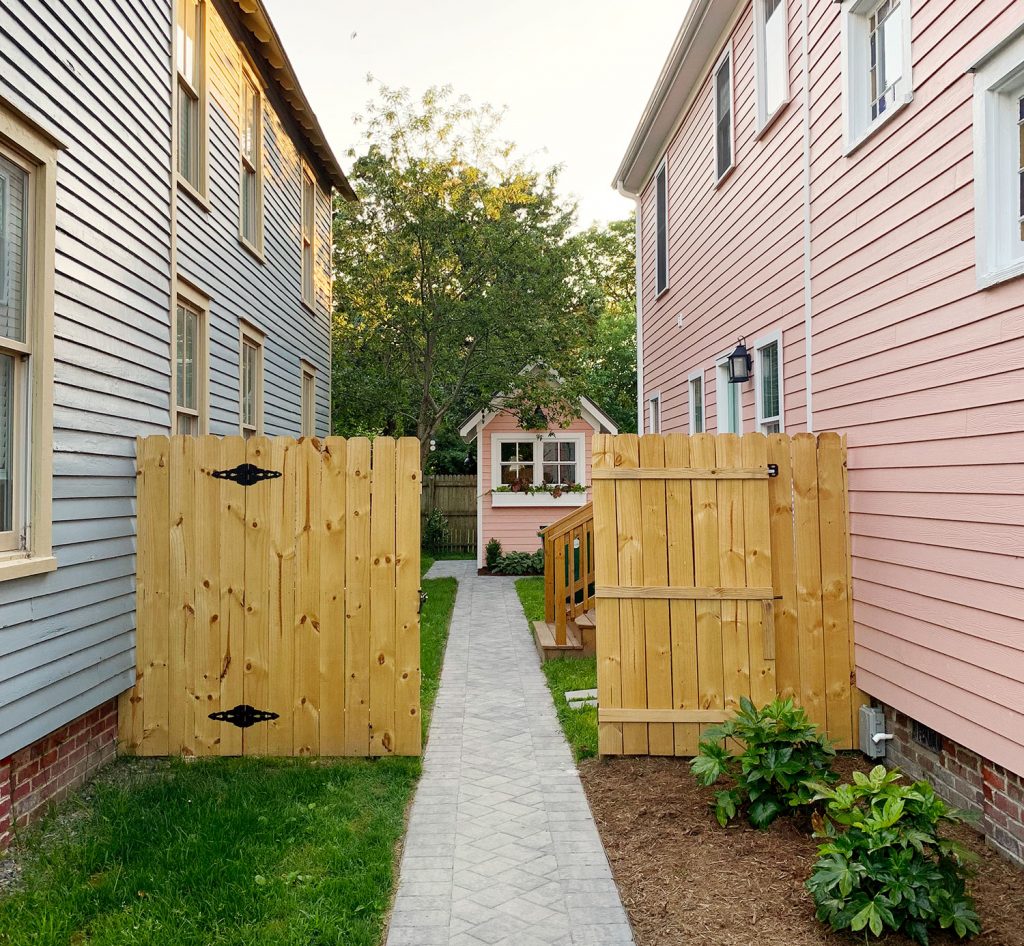 Wood Fence Added On Side Yard Of Historic Beach Homes With Paver Stone Pathway Leading to Backyard Shed