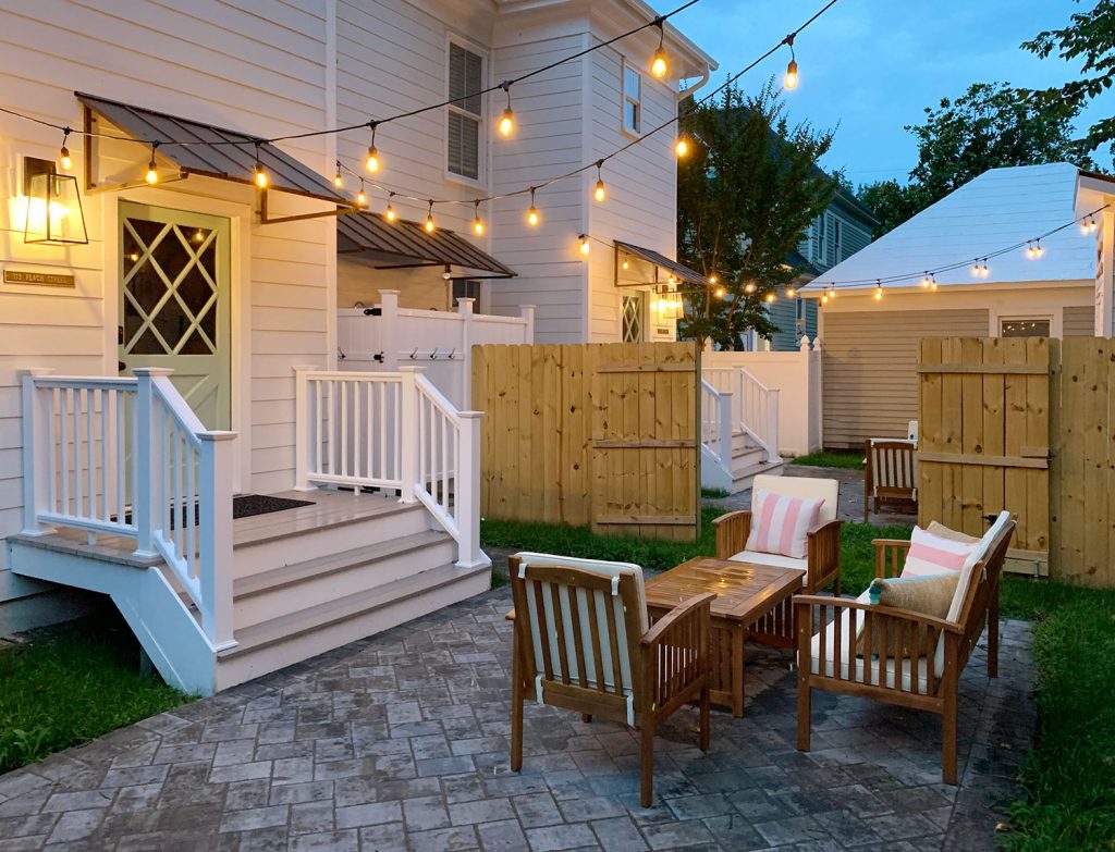 Duplex Back Yard With String Lights And Matching Patio Areas Separated By Wood Fence