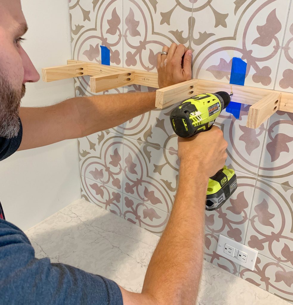 Man Drilling Through Tile Backsplash With Wood Support Bracket Held Up