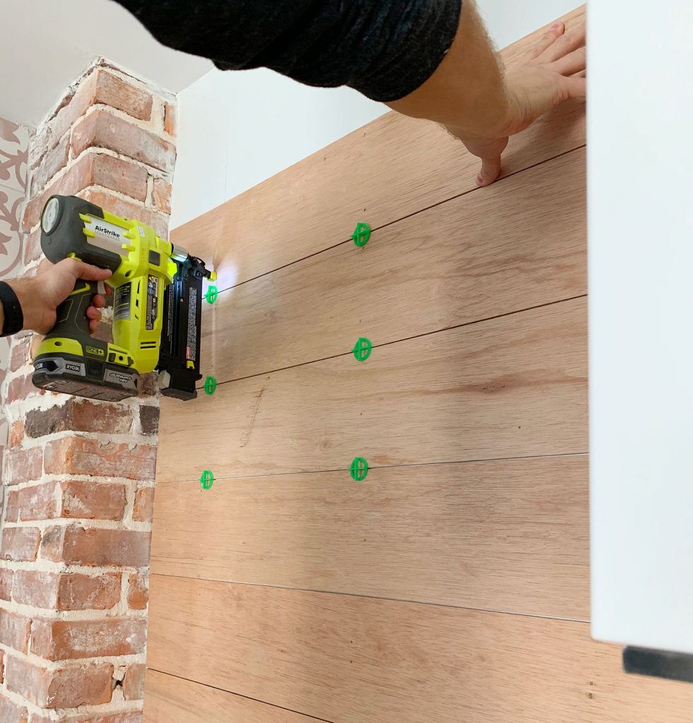 Nail Gun Securing Wood Panels To Backsplash Using Tile Spacers