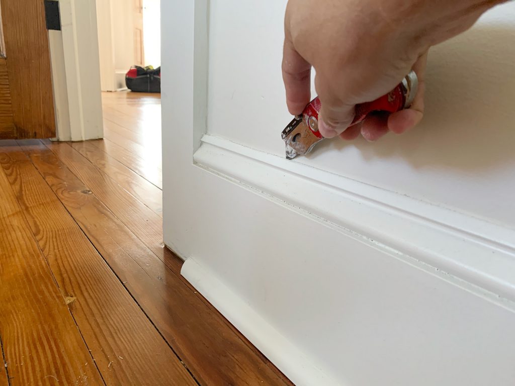 Utility Knife Cutting Caulk Paint Line Before Detaching Old Baseboard