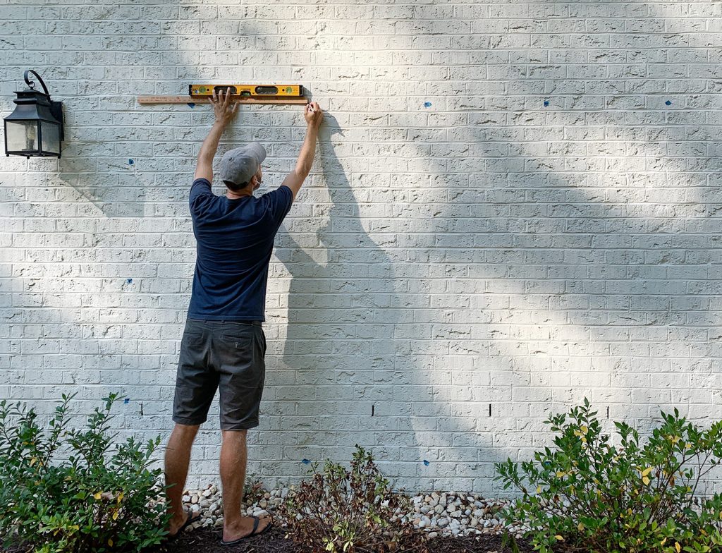 John Marking Trellis Hooks On Brick Wall (Marcando ganchos de treliça na parede de tijolos)