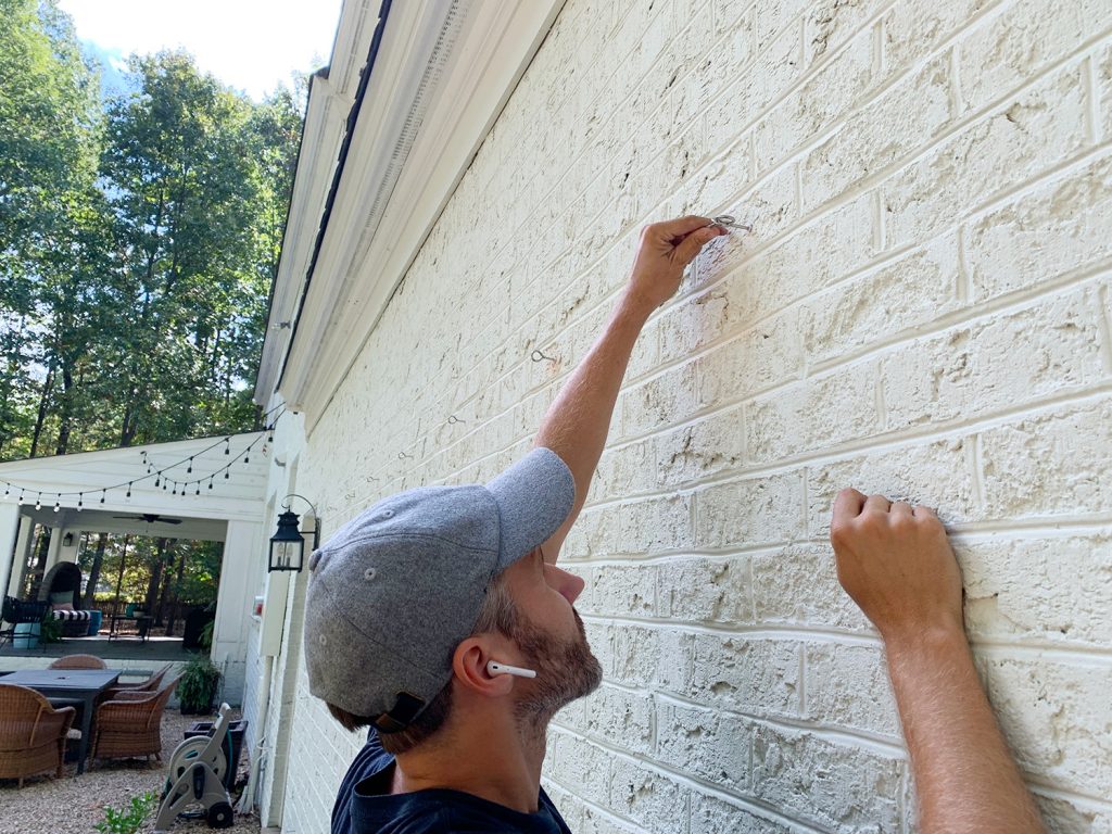 John Screwing In Eye Hooks On Brick Wall