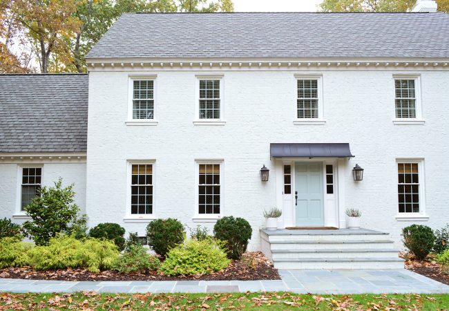 Painted Brick Colonial Home With Metal Awning And Blue Stone Walkway