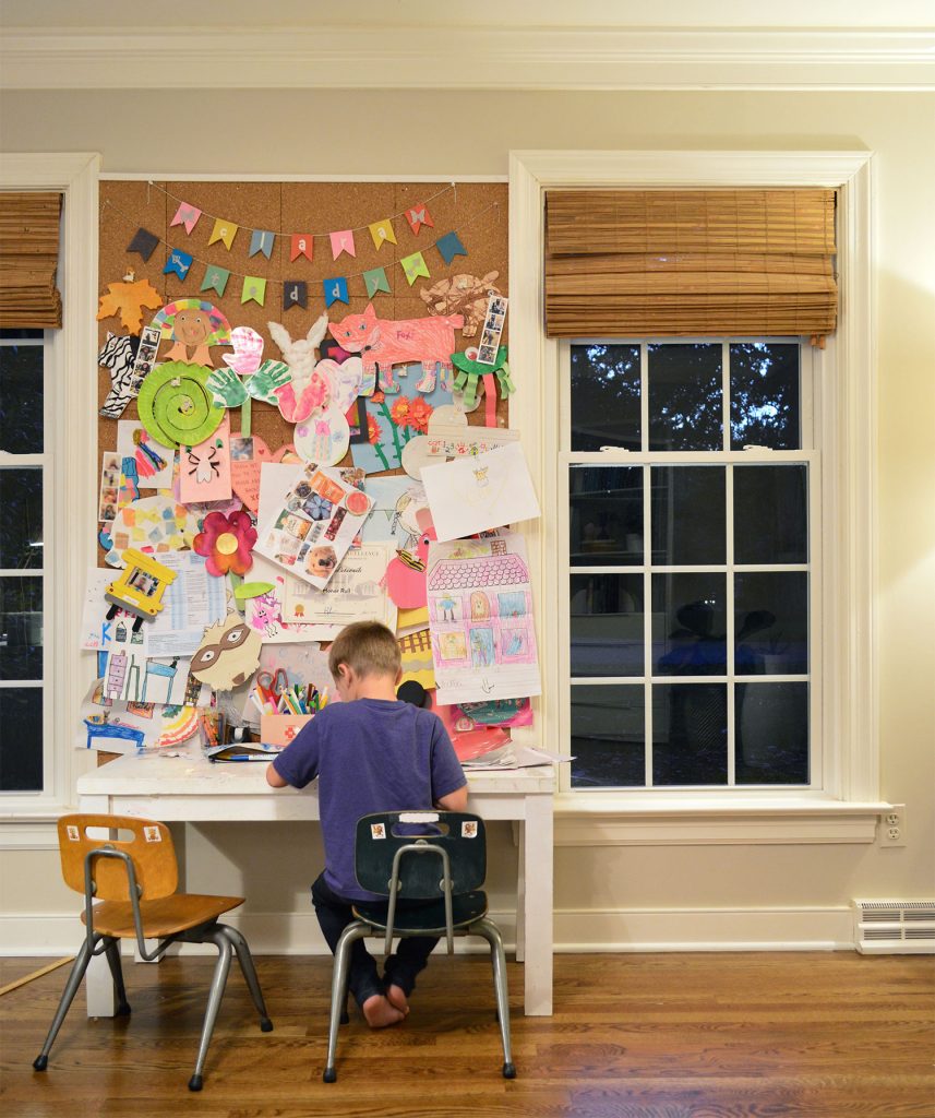 Son Working At Small Art Desk Space In Preschool Chairs With Large Corkboard Display Space Between Windows