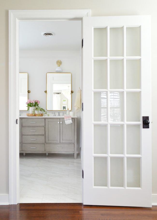 After Photo Of View Into Bathroom With Marble Floor And Gray Double Vanity And Gold Mirrors