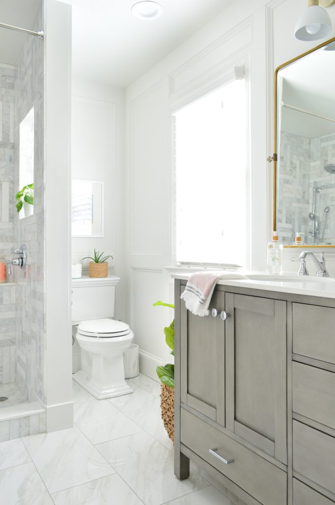 View of toilet in back corner of marble bathroom with gray vanity