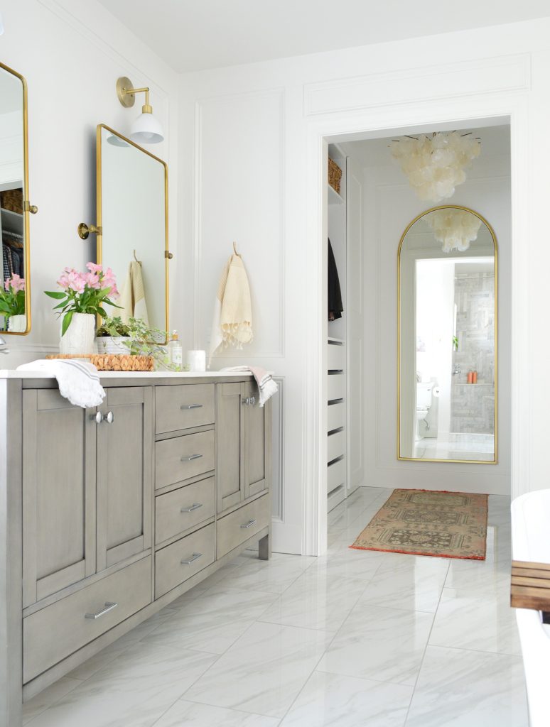 Double Gray Bathroom Vanity Next To Entrance To Large Walk-In Closet With Arch Mirror