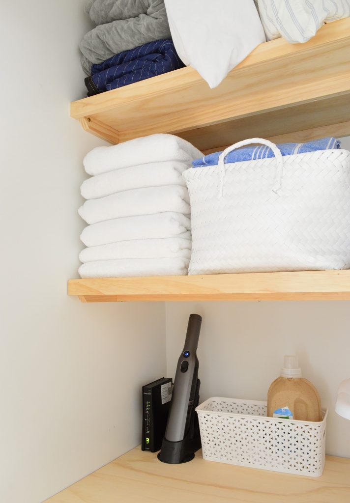 Towels and baskets stored on wood laundry shelves with support braces underneath