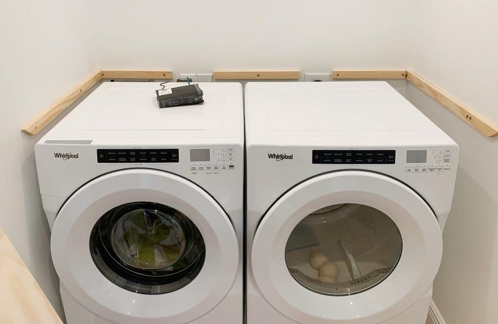 Wood laundry shelf supports added to walls besides washer and dryer