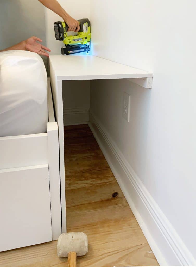 Painted pieces of MDF being nailed in for bottom shelf of built-in bookcase