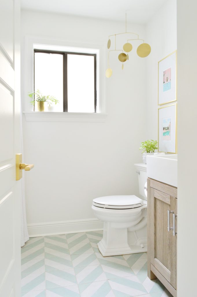 White bathroom with green tile floor and gold mobile