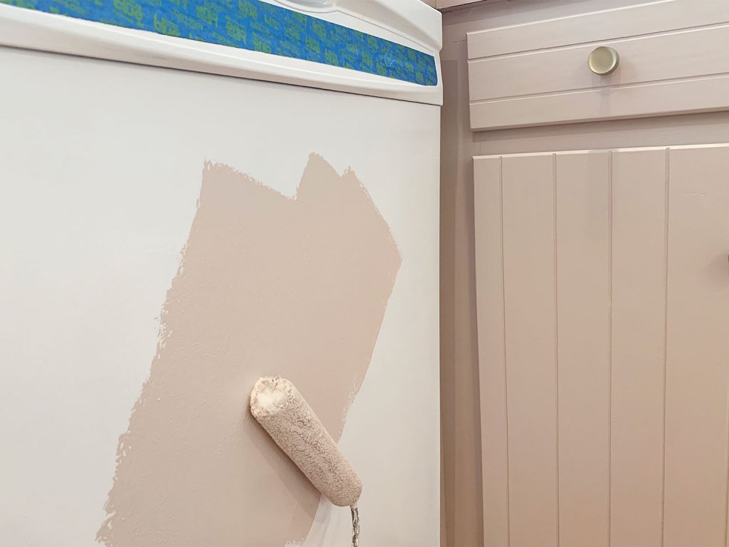 Rolling mauve paint onto white dishwasher using small foam roller