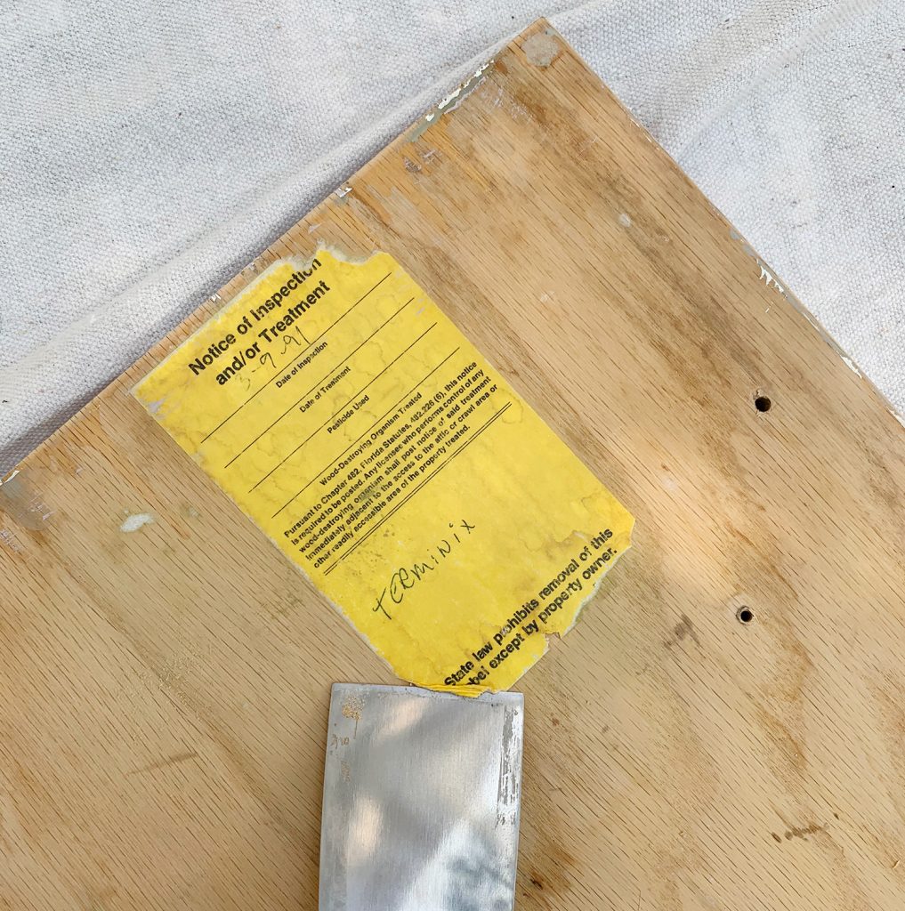 Scraping old label off the back of kitchen cabinets as painting prep