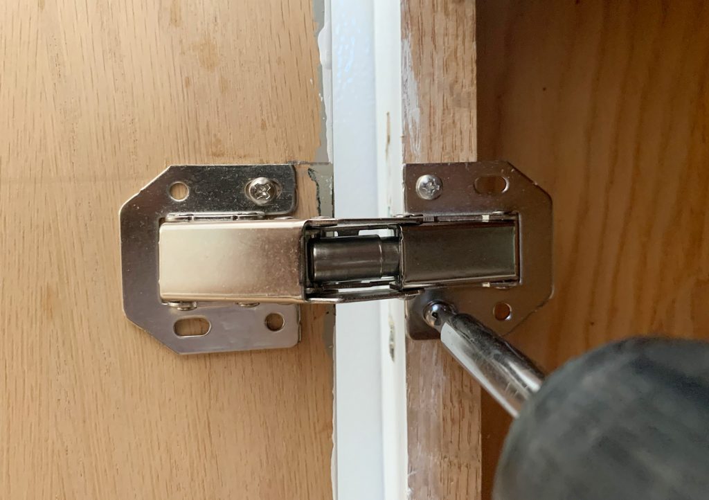 Screwing hidden hinge onto cabinet frame in kitchen renovation