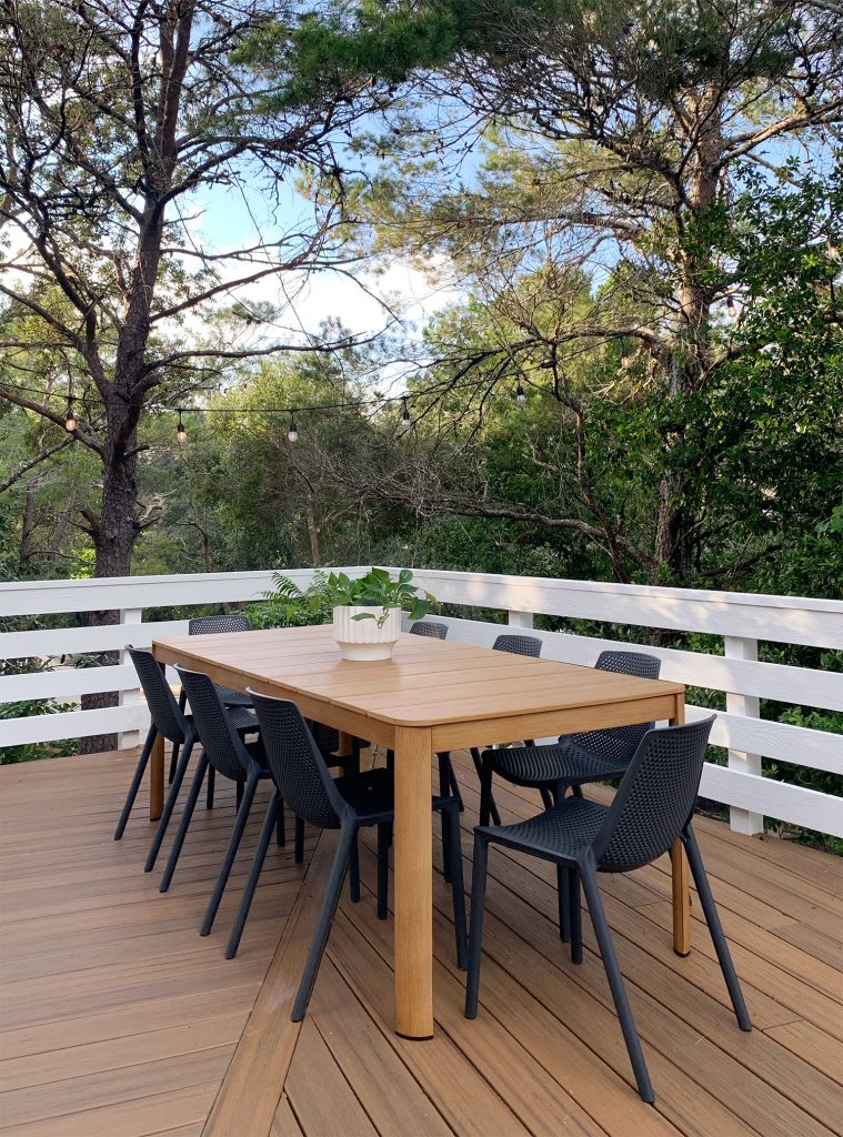 Mesa de jantar externa de metal com madeira falsa e cadeiras pretas cercadas por árvores