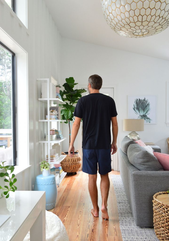 Man In Black Shirt Walking In Living Room Under Large Light Fixture