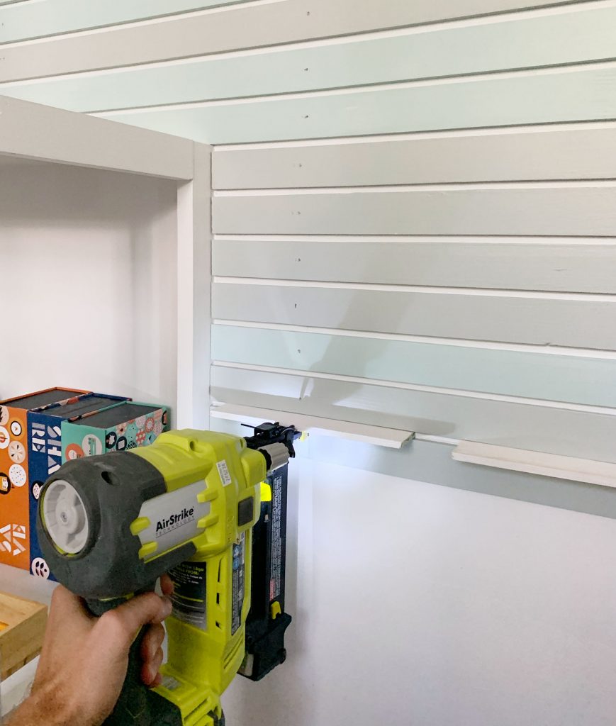 Nail Gun Attaching Smaller Lattice Pieces Onto Wall Next To Bookshelf