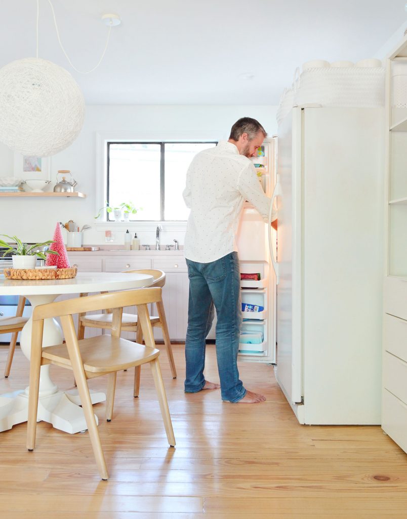 John standing with freezer door open next to round table in kitchen