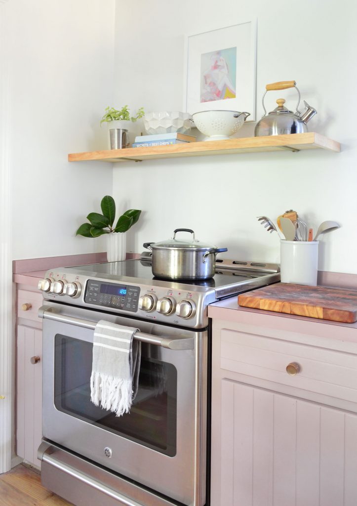 Stainless steel electric stove with mauve cabinets and floating wood shelf