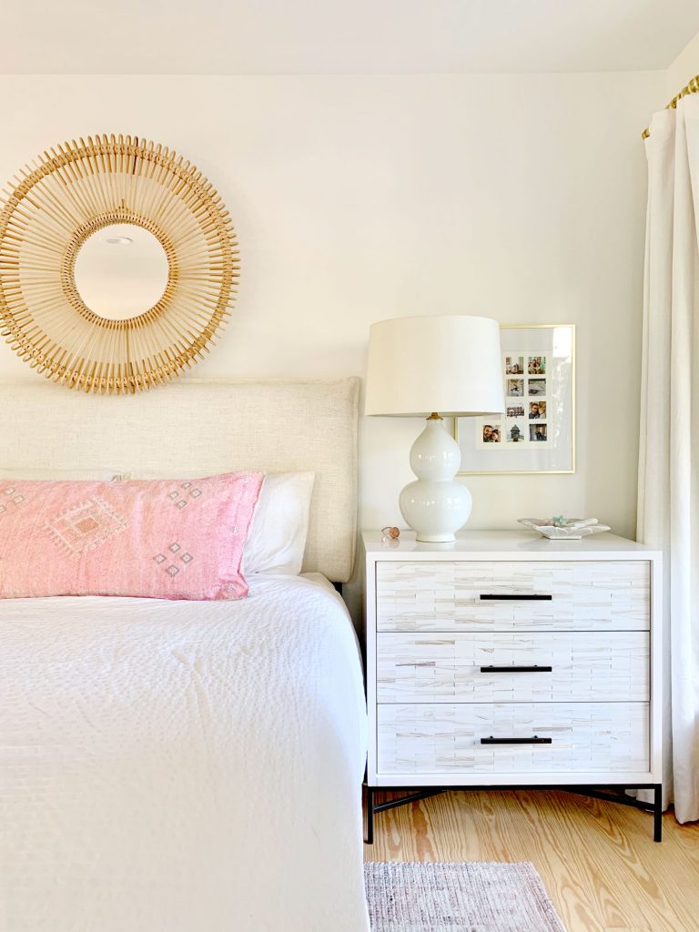 Linen headboard on bed with white bedding and inlay dresser as nightstand