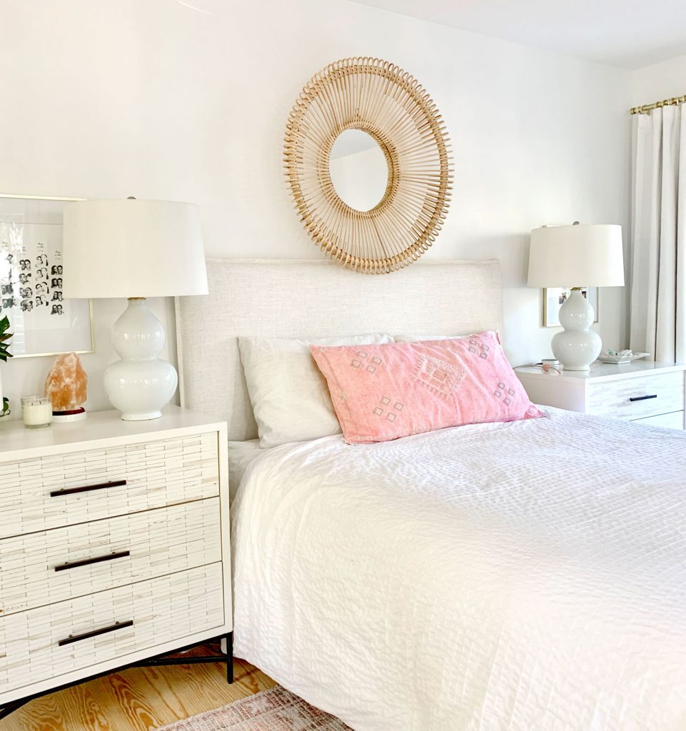 Linen headboard on bed with white bedding and round wicker mirror over headboard