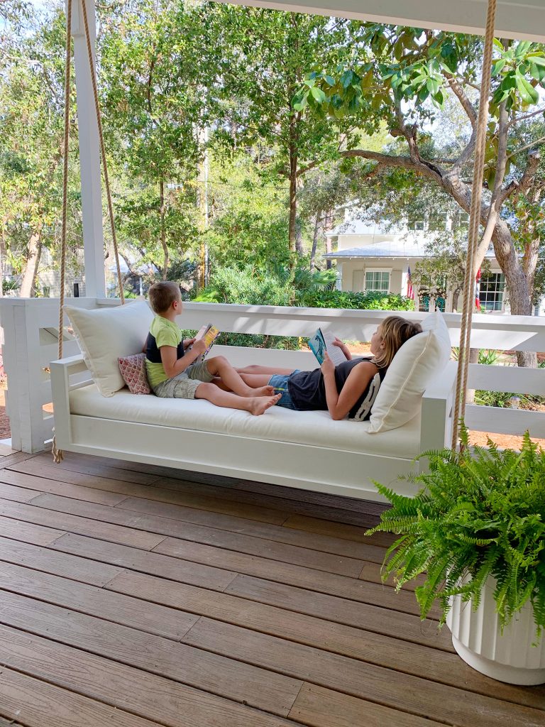 Two Kids Reading On Either End Of White Hanging Daybed Swing