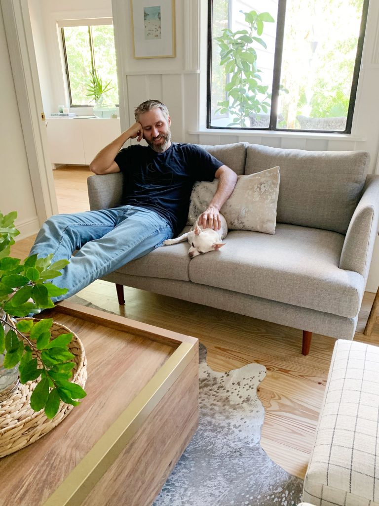 John sitting on gray loveseat with chihuahua next to him