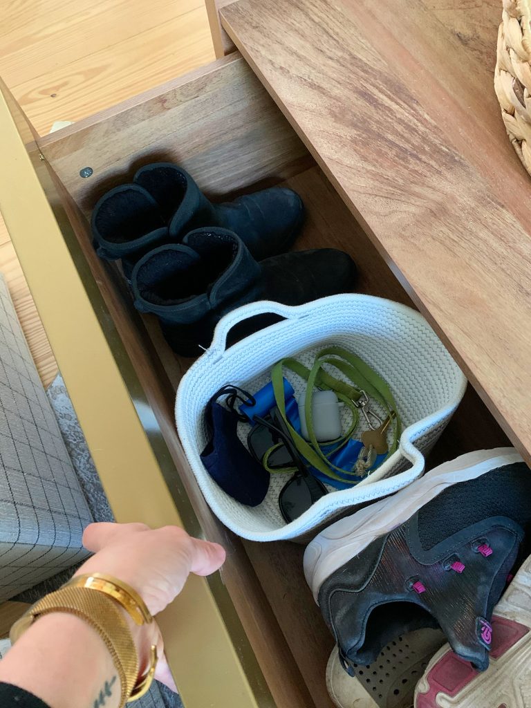 Open drawer of wood storage coffee table showing shoes and basket with keys