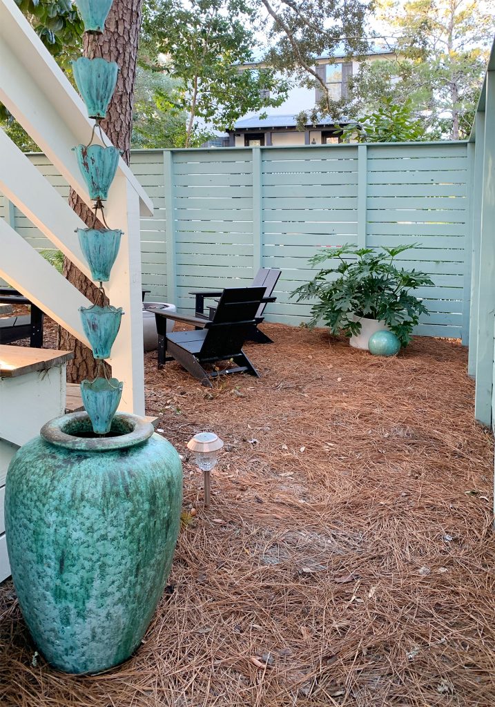 View through gate fence next to blue-green pot and rain chain