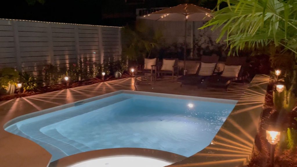 Small freeform pool at night with pool lights and solar lights on
