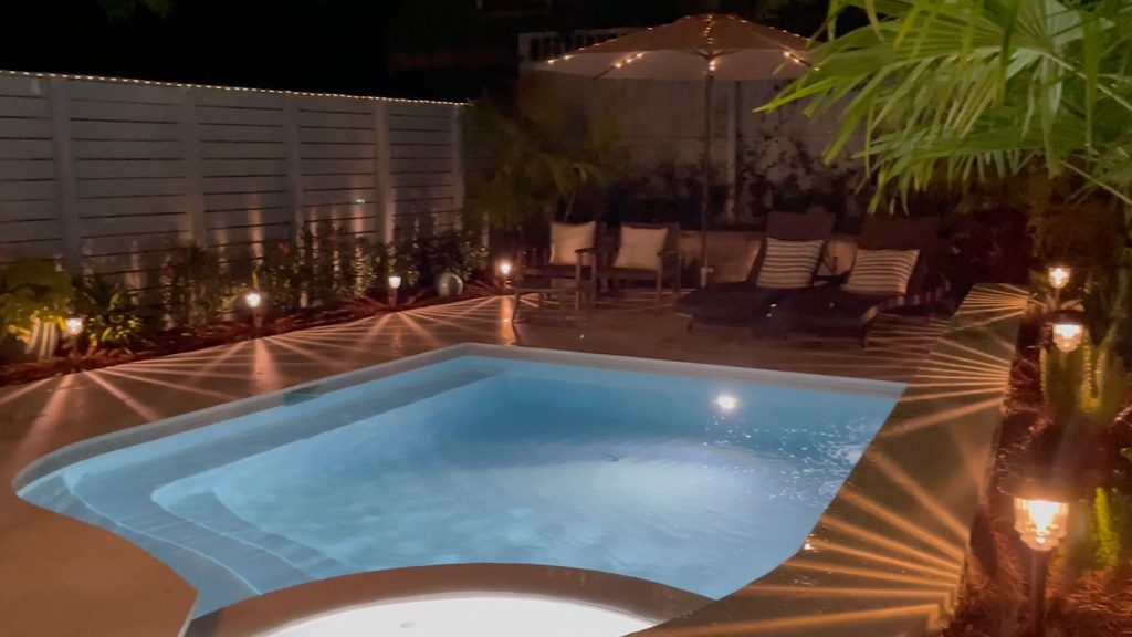 Pequena piscina de forma livre à noite com luzes de piscina e luzes solares acesas