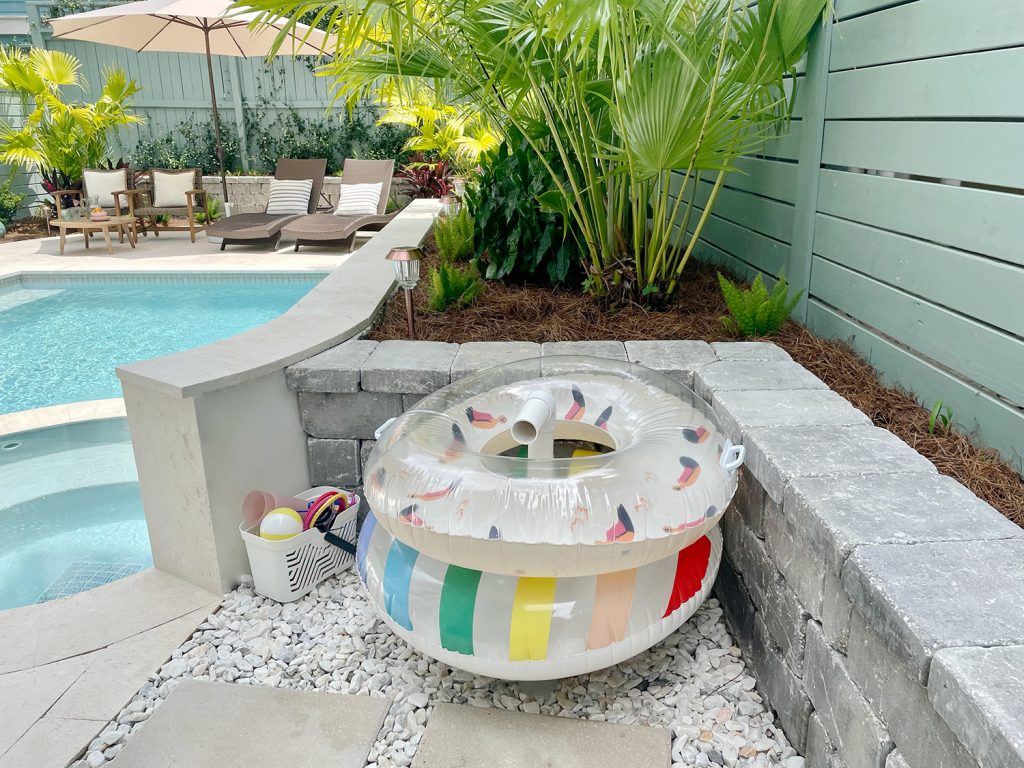 Pool floats organized on PVC pipe stand behind retaining wall