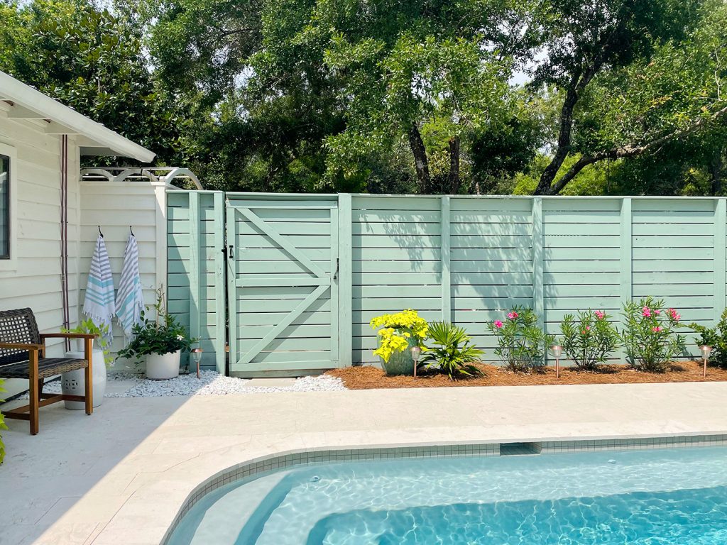 Cerca da piscina com ripas horizontais e pintura verde cinza com canteiro de plantio na frente