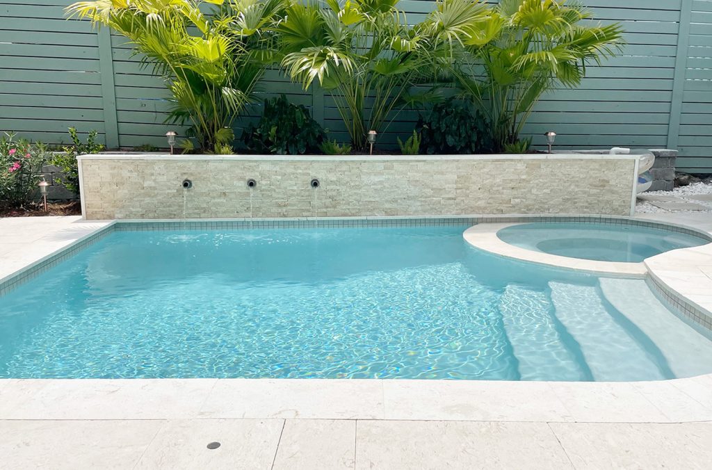 Small freeform pool with accent stone tile retaining wall flanked by gray block retaining wall