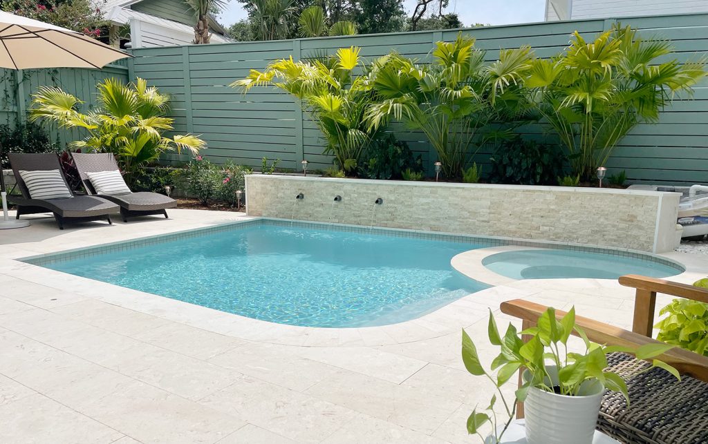 Piscina pequena no quintal com borda curva e plantas de palmeira atrás do muro de contenção