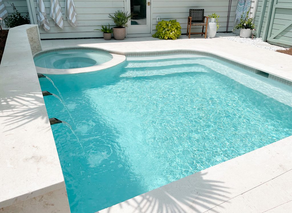 Vista em ângulo de uma pequena piscina de forma livre com escada em uma extremidade e banco em uma extremidade mostrando o gesso Ivory DiamondBrite