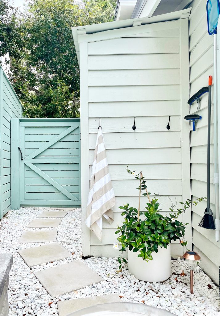 Hook towel storage along white shed and pool skimmer hanging on hooks on house siding