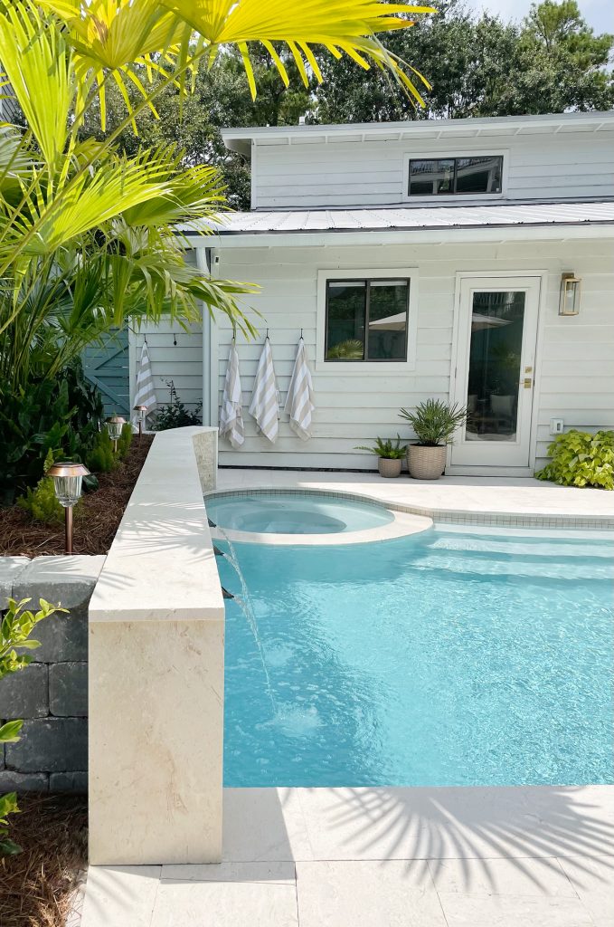 Side view of pool accent wall with fountain sprayers and round spa in background