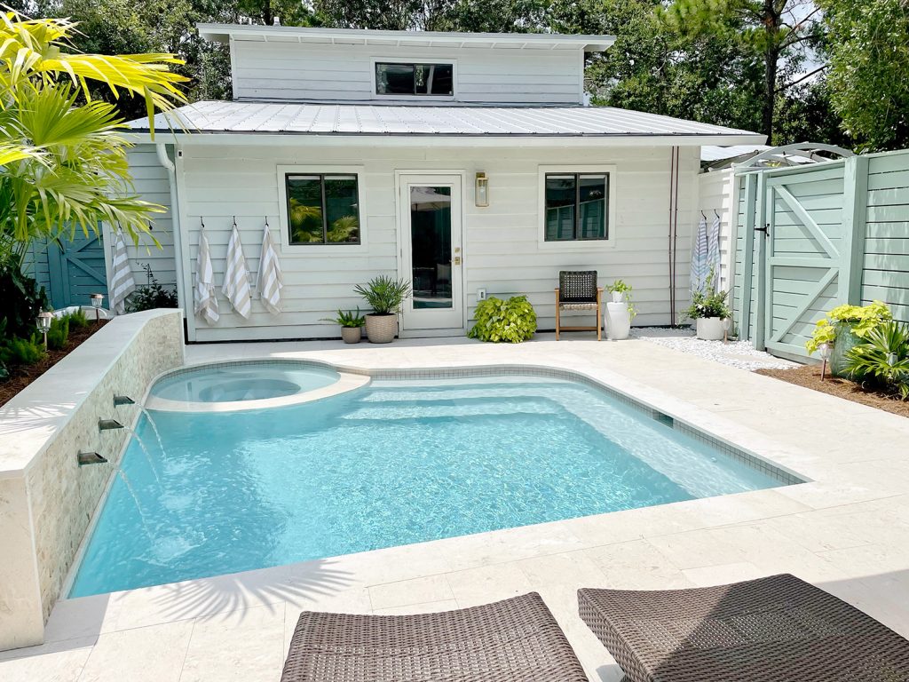 Pequena piscina de forma livre no quintal atrás de uma casa moderna branca