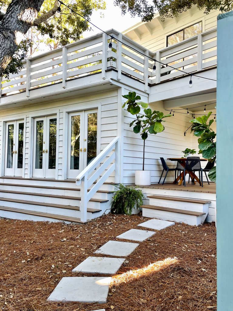 Angled view through fence gate at side porch yard area with doors to bedroom